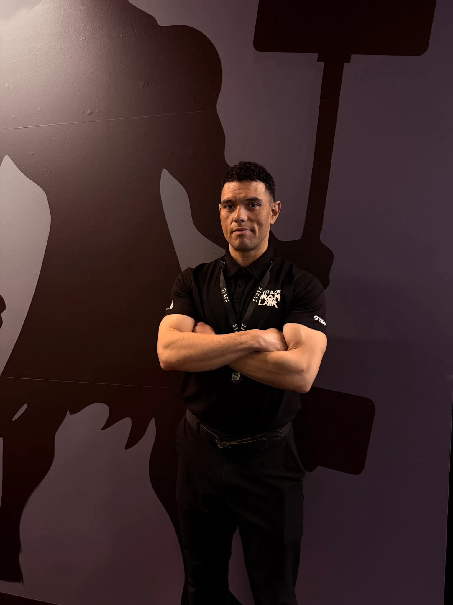 Andrew Rodriguez in an Athlos Iron Lair polo, arms folded, photographed against a dark wall.