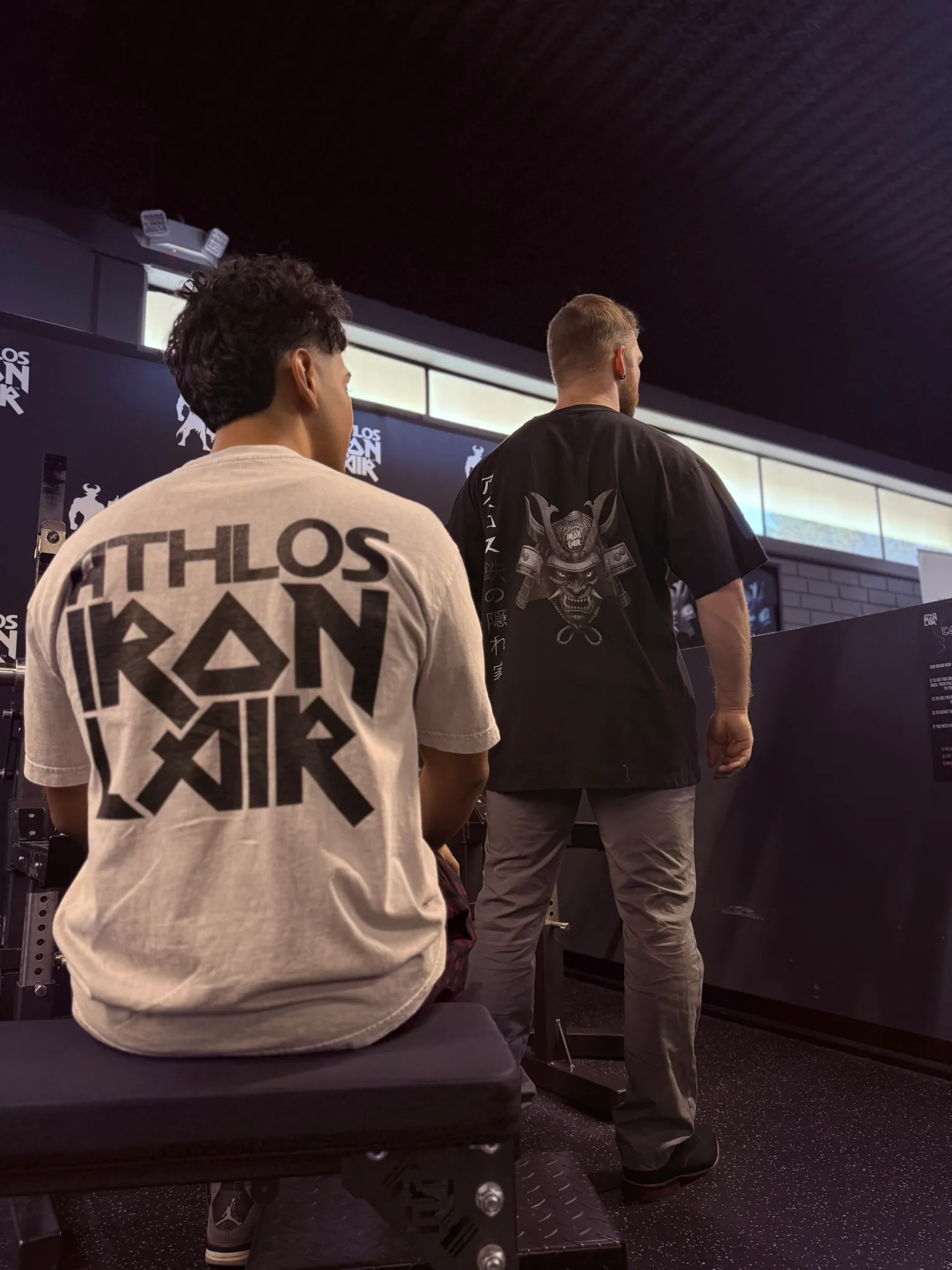 Two members in Athlos Iron Lair shirts on the floor, seen from behind.