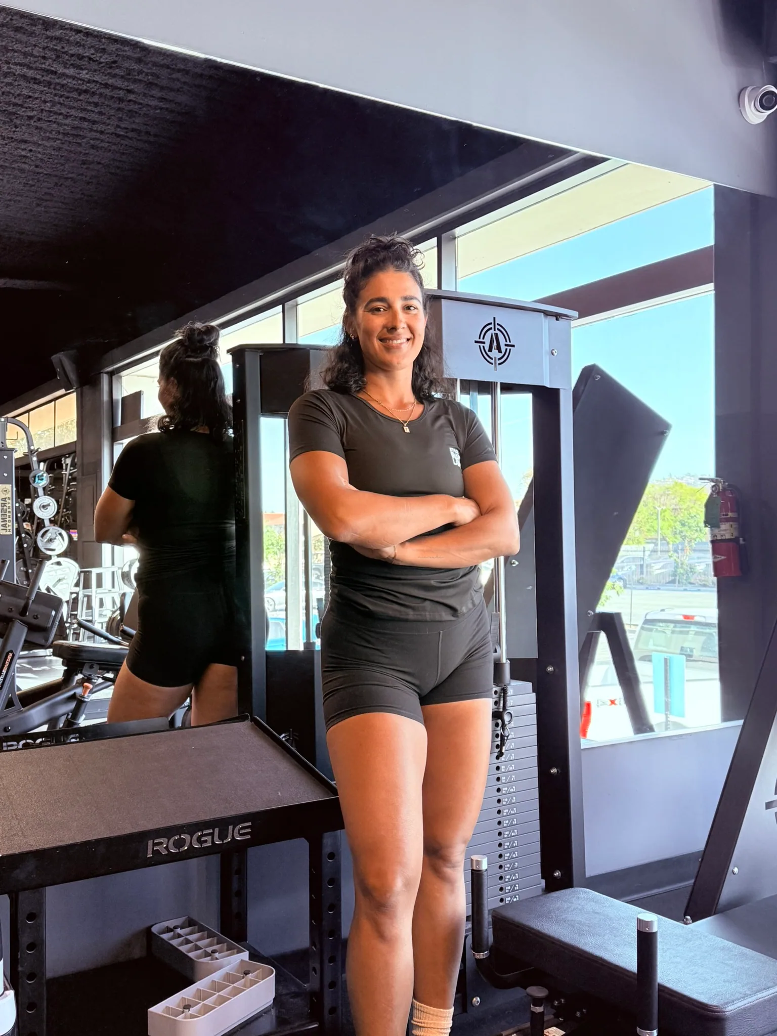 Tessa Weller standing beside a Rogue rack with the windows behind her, arms folded.