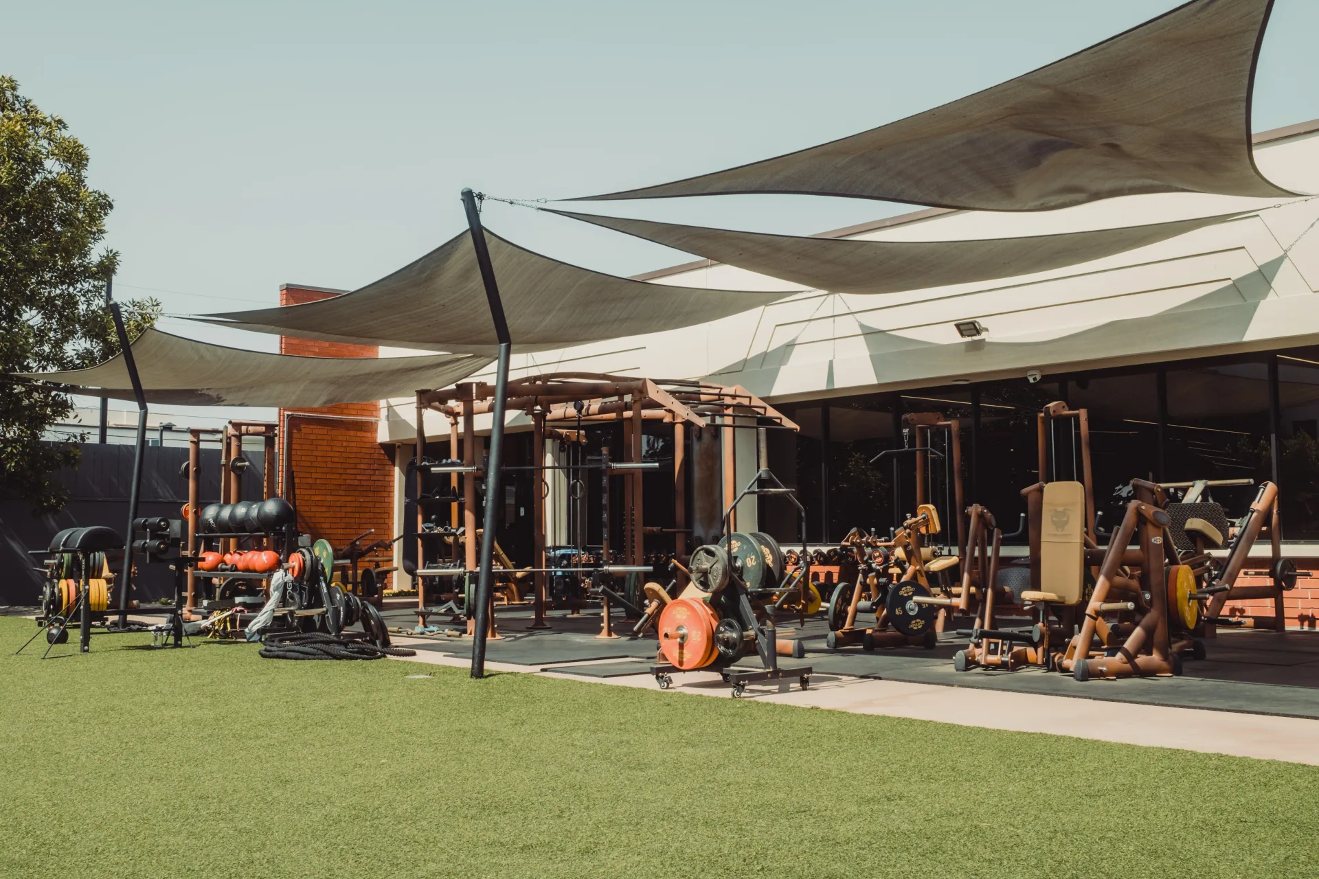 The outdoor training area under shade sails, with sleds, plate-loaded machines and turf