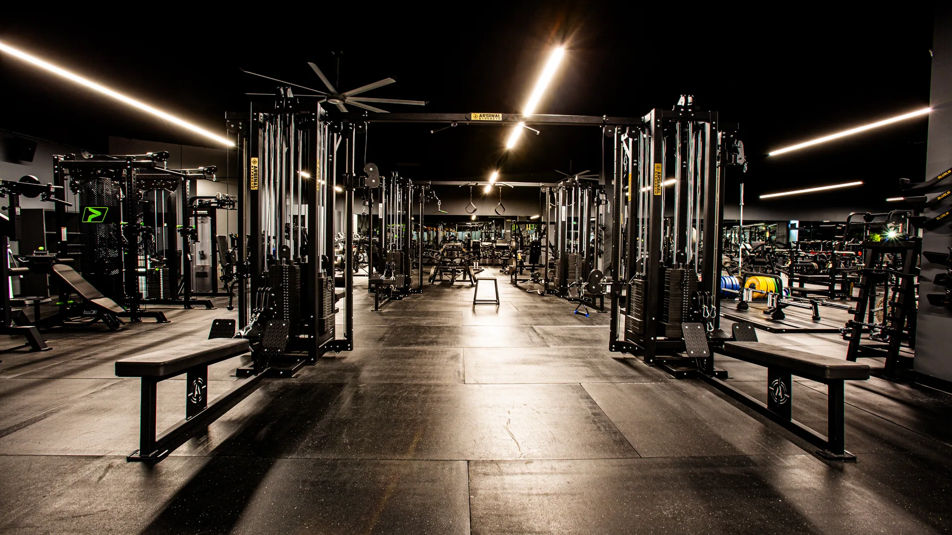 Benches and squat racks receding down the floor under strip lighting