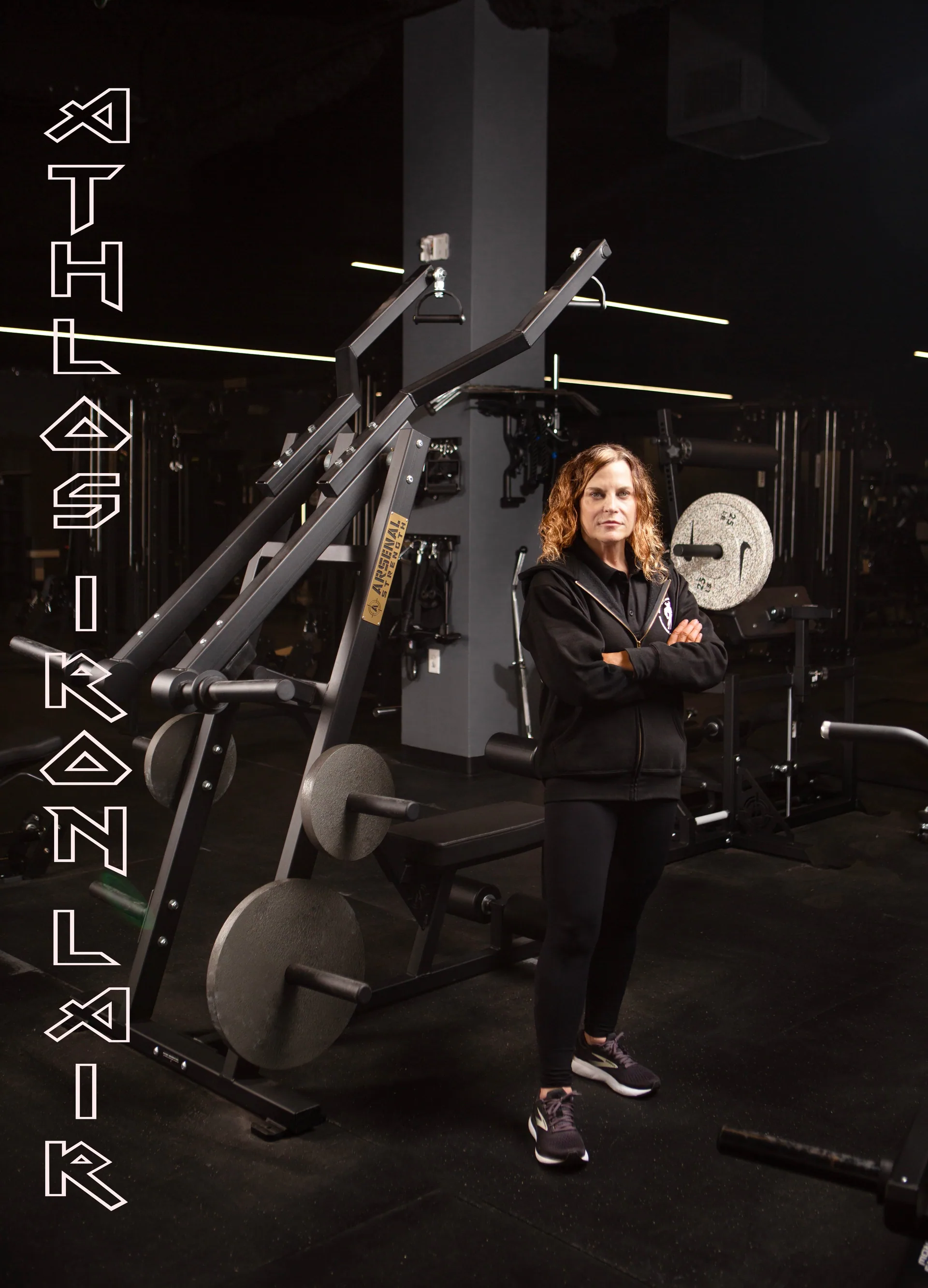 Member standing at a functional trainer in front of the Athlos Iron Lair wall mural