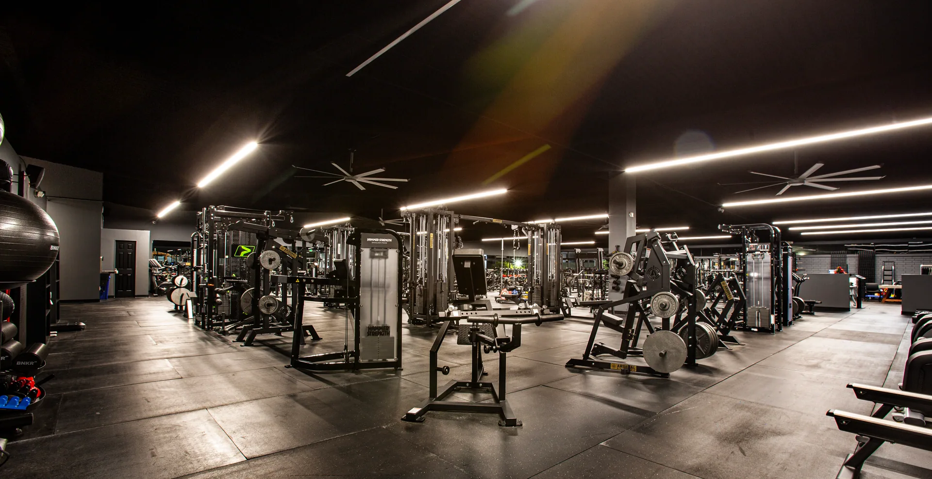 Wide view down the main training floor, machines and ceiling fans overhead